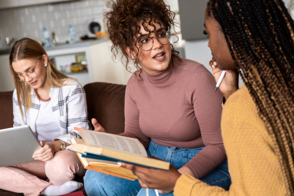 Diverse group female students learning at home using laptop and books for research.