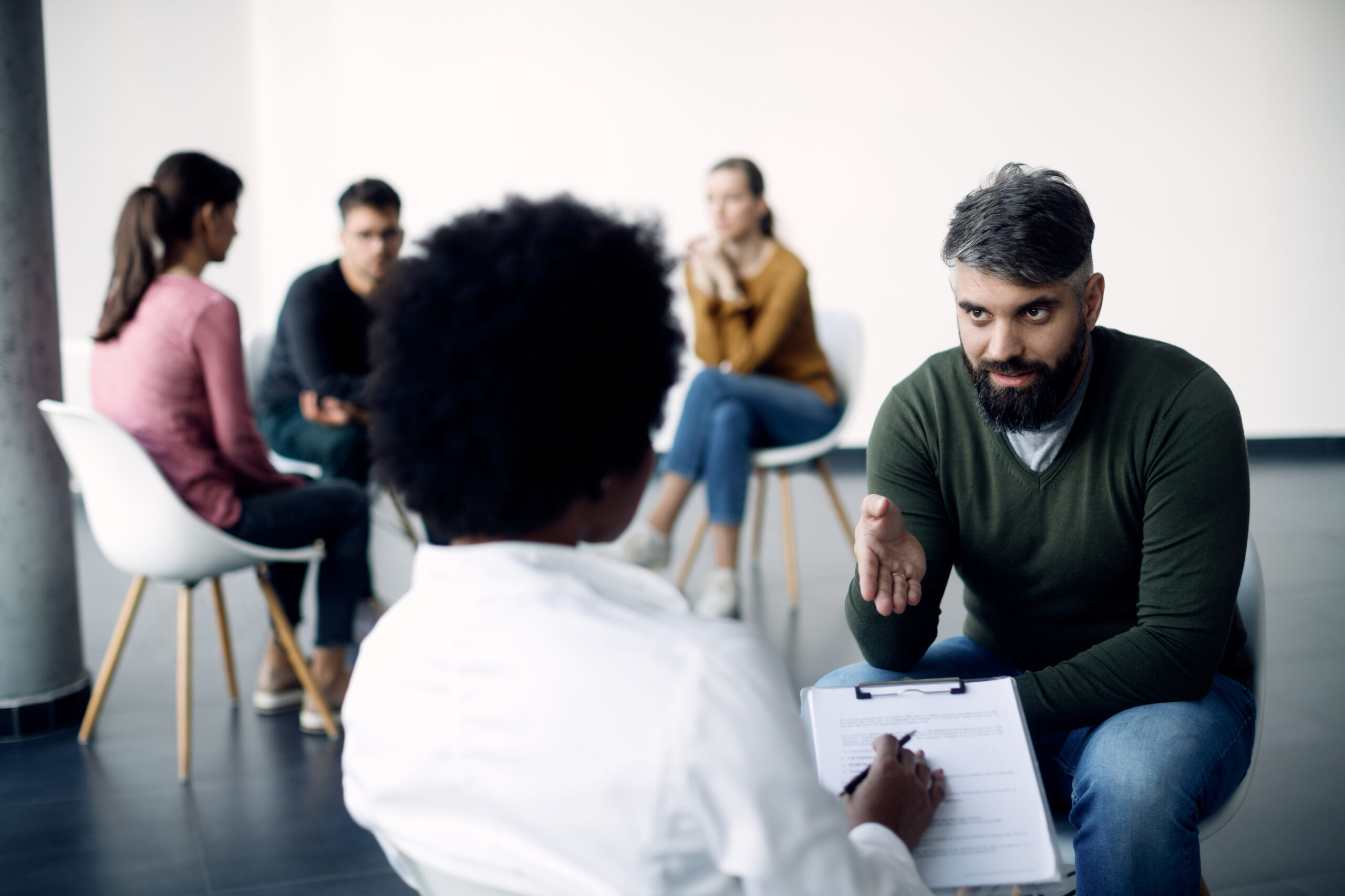 Mid adult man attending a group therapy and communicating with female doctor at medical center.