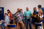 Three-quarter-length shot of a group of adults standing in a circle and talking to each other about their mental well-being. There is a staff member sitting to the left of them in the frame sitting next to a table. The community centre is located in Seaton Deleval in the North East of England.